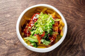 Wall Mural - golden French fries in a white bowl, generously topped with ketchup, two meat sausage and fresh green herbs on a rustic wooden surface