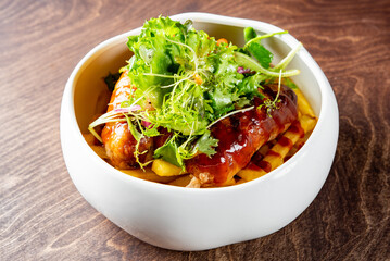 Wall Mural - golden French fries in a white bowl, generously topped with ketchup, two meat sausage and fresh green herbs on a rustic wooden surface