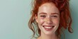 Place for text. A beautiful young red-haired girl with freckles smiles a radiant smile on a green background. Suitable for advertising dentistry, beauty industry, advertising lenses