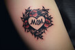 Red heart shaped tattoo with flowers with text 'MOM' on person's arm