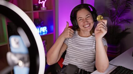 Canvas Print - Thumbs up! joyful young woman with blue eyes records her bitcoin success video in a gaming room, radiating positivity with her cheerful smile