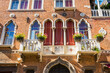 Facade of old building with typical Venetian windows and white balcony with flower pots. Venice, Italy