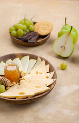 Wall Mural - Cheese on a wooden board next to fruit on a beige background