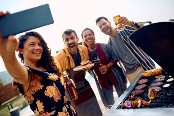 Cheerful friends taking selfie while having BBQ party outdoors.