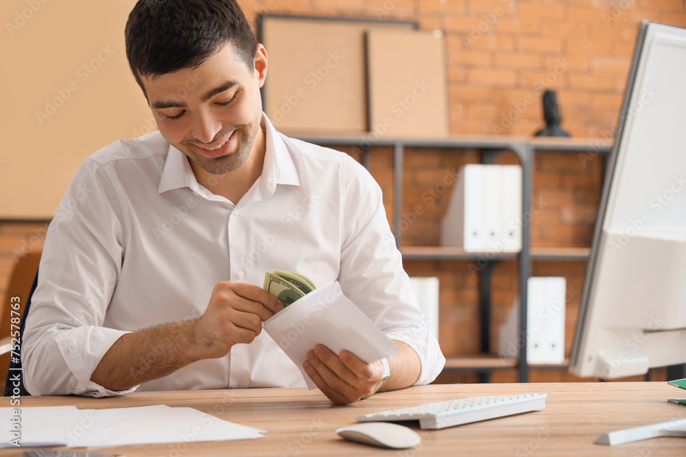 Young businessman with envelope of money in office
