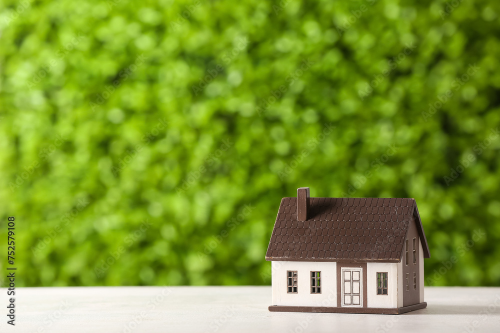 House figure on white table against decorative green grass. Concept of buying real estate