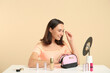 © Pixel-Shot - Beautiful young woman with cosmetic bag full of makeup products doing makeup at table on beige background