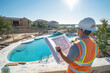 © Александр Марченко - A construction engineer in a reflective vest and hard hat reviews blueprints at a residential pool construction site.