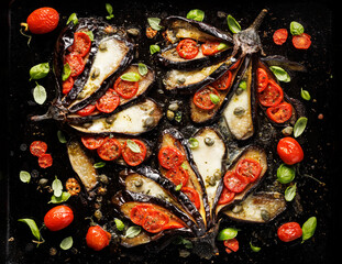 Wall Mural - Baked eggplants in the fan shape stuffed with cherry tomatoes and mozzarella cheese on a black background, top view