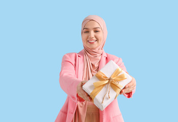 Poster - Young Muslim woman with gift on blue background. Ramadan celebration