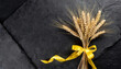 Golden ears of wheat bouquet  with yellow ribbon placed on textured black stone plank