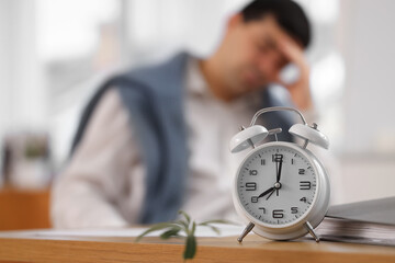 Canvas Print - Alarm clock on table of stressed businessman in office, closeup