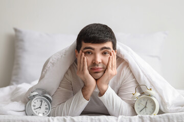 Wall Mural - Young man with alarm clocks lying in bedroom, closeup