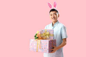 Sticker - Young Asian man in bunny ears with gifts on pink background. Easter Sale