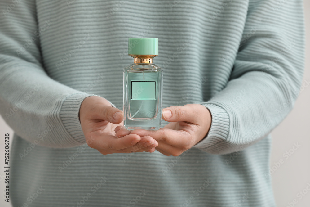 Woman holding perfume bottle on grey background, closeup