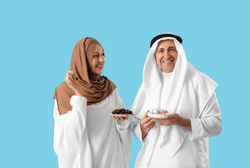 Wall Mural - Happy Muslim couple with traditional sweets on blue background. Eid al-Fitr celebration