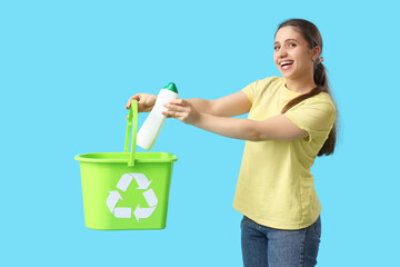 Young woman throwing plastic bottle into recycle bin on blue background. Waste sorting concept