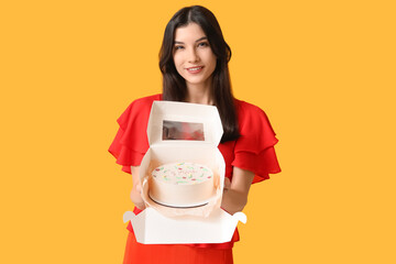 Wall Mural - Beautiful young woman holding box with sweet bento cake on yellow background. International Women's Day