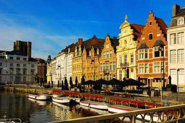 Wall Mural - Scenic cityscape of Ghent with traditional Flemish style brick townhouses decorated with colorful blooming flowers on banks of Leie river on sunny summer day, Belgium.