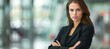 Confident businesswoman in office, arms crossed, blurred background, space for text