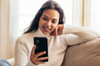 © PEDROMERINO - Connected at Home: Young Woman Sitting on Sofa Using Smartphone
