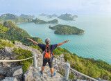 Fototapeta Kosmos - The man with backpack  raised up arms celebrate standing on high cliff Pha Jun Jaras view point the peak of mountain at Wua Ta Lap island Surat Thani, Thailand