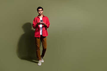 Wall Mural - Full length photo of funny good mood man dressed red shirt walking texting modern device empty space isolated green color background