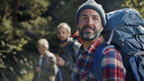 Fototapeta  - Hikers with backpacks trekking in a sunlit forest, with focus on a bearded man in the lead.