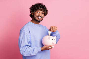 Photo of positive rich man wear trendy blue clothes hold piggy box save money for future isolated on pink color background