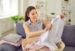 © Studio Romantic - Happy young housewife looking at just washed clothes. Beautiful young woman sitting on couch with laundry basket, looking at perfectly clean, white shirt with no stains and smiling