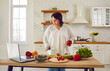 © Studio Romantic - Portrait of fat overweight young woman preparing fresh vegetable salad looking at recipes on a laptop standing in the kitchen at home. Diet restrictions, healthy eating and diet, weigh loss concept.