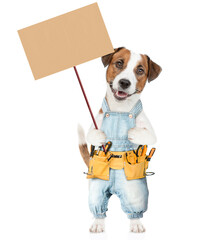 Poster - Funny Jack russell terrier puppy wearing denim overalls with tool belt holds adjustable wrench and shows empty placard. isolated on white background