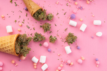 Wall Mural - Dry buds of medical marijuana lie on waffle ice cream cones on a pink background.  There are candies and marshmallows . around.  Alternative medical cannabis treatment