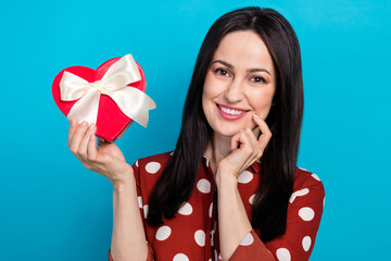 Sticker - Portrait of minded dreamy girl with brunette hair wear red shirt hold heart gift box finger on chin isolated on blue color background