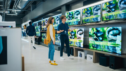 Wall Mural - Beautiful Female Client Having a Conversation with Retail Home Electronics Shop Consultant. Young Woman is Shopping for a Modern TV Set. Customer Looking for a New Television in Department Store