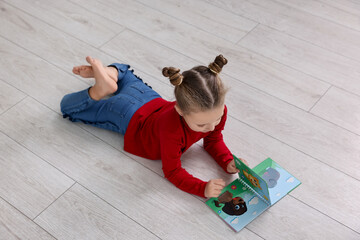 Wall Mural - Cute little girl reading book on warm floor indoors. Heating system