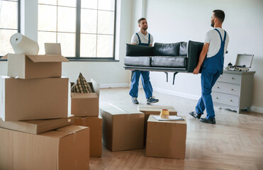 Holding heavy sofa. Two moving service employees in a room