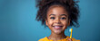 smiling black kid girl child holds toothbrush in hand on blue isolated background. Pediatric dentistry for brushing teeth