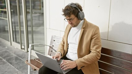 Poster - Young man with headphones using laptop on city bench