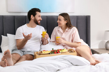 Wall Mural - Happy couple having breakfast and talking on bed at home