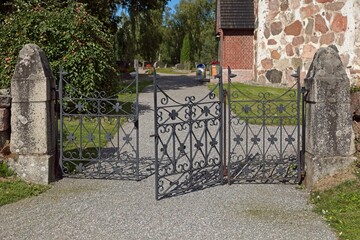 Old ornamental wrought-iron gate with crosses to cemetery in summer.