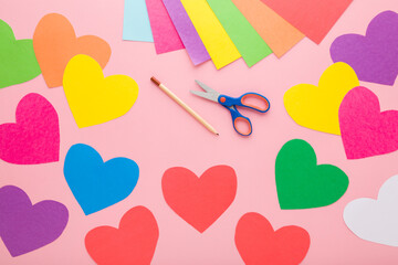 Wall Mural - Colorful heart shapes, scissors, pencil and application paper on light pink table background. Pastel color. Closeup. Making decoration elements. Top down view.