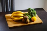 Fototapeta Kuchnia - Warzywa i owoce leżą na desce do krojenia. Brokuł, banany, kiwi i cytryna.