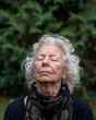 Photo of a senior woman practicing meditation in a peaceful garden, with a close-up on her serene, focused face reflecting inner peace