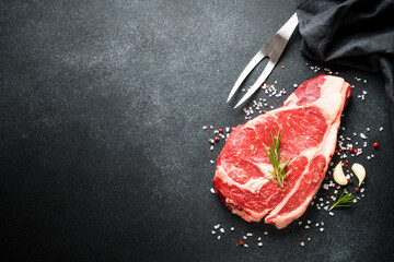 Poster - Beef steak with spices on black background. Ribeye steak raw meat. Top view with copy space.