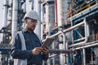© charnsitr - Male engineer with tablet in front of oil refinery