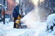 A man clears snowdrifts with a snow blower on a city street on a winter day.