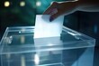 A voter's hand places a ballot into a transparent glass ballot box for an election.