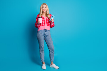 Sticker - Full length photo of cheerful adorable woman dressed pink jumper hold to go latte smartphone in hands isolated on blue color background