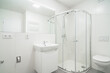 Bright white small bathroom with sink, wc and shower. The bathroom has a large mirror with LED strip, toilet flush button, heating ladder, few outlets and water with waste for the washing machine.
